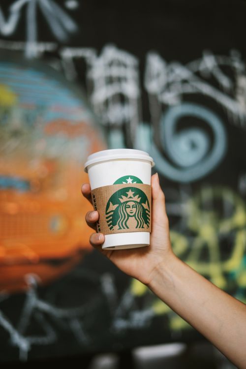 Free Close-up of a hand holding a coffee cup against a vibrant graffiti wall. Stock Photo