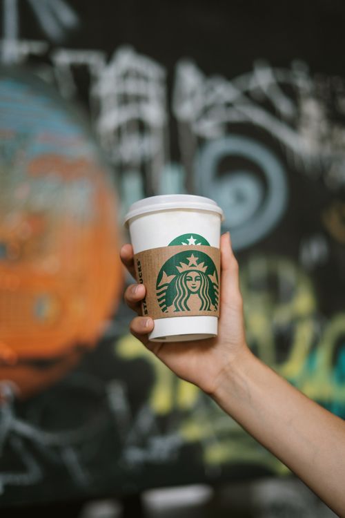 Free A hand holds a Starbucks cup against a colorful graffiti background, emphasizing urban style and coffee culture. Stock Photo