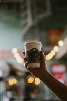 Close-up of a hand holding a Starbucks coffee cup with a blurred cafe background.