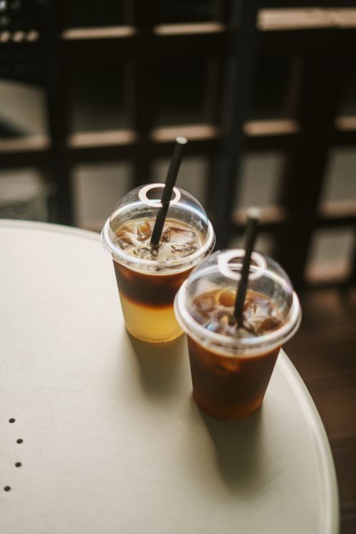 Free Two iced beverages in plastic cups with straws on a sunny day outdoor table. Stock Photo