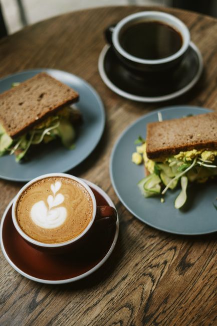 A cozy setting featuring a cappuccino with latte art and sandwiches on plates, ideal for a coffee break.