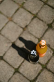 Overhead view of two soda bottles casting shadows on cobblestone pavement.
