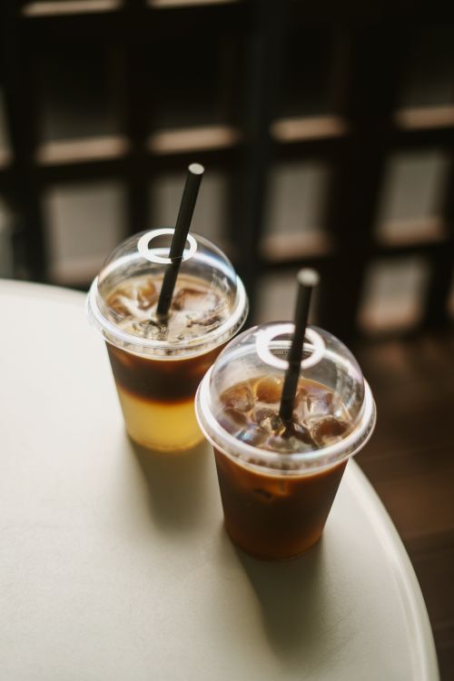Free Two iced coffee drinks in clear plastic cups with straws on a cafe table, softly lit. Stock Photo