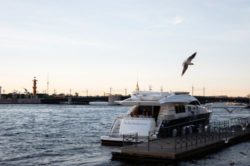 Free Elegant yacht docked at a pier in Saint Petersburg, with seagulls flying overhead and iconic architecture nearby. Stock Photo