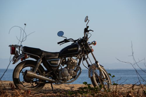 Free Vintage motorcycle parked on a sandy seaside path with a clear blue sky backdrop. Stock Photo