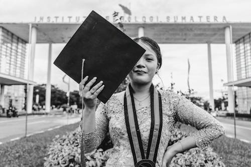 Grayscale Photo of Woman Holding a Graduation Hat