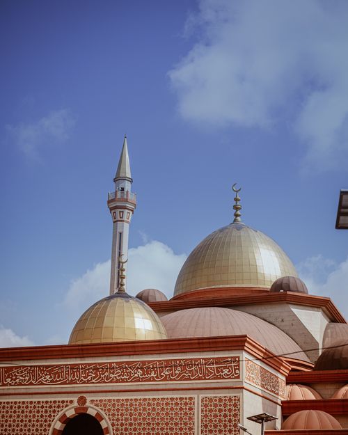 Free A stunning mosque with golden domes and a minaret under a vibrant blue sky. Stock Photo