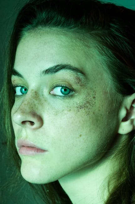 Artistic close-up portrait of a woman highlighting freckles and green eyes with a soft moody tone.