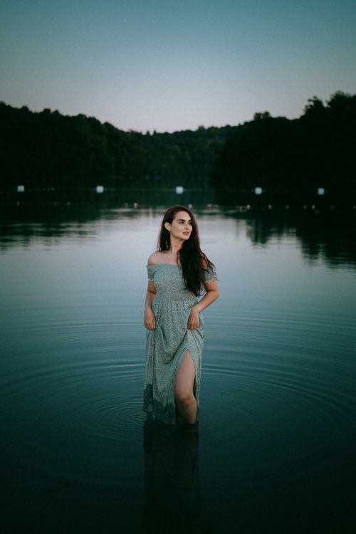 Free A serene portrait of a woman standing in a lake at dusk, reflecting calm and beauty. Stock Photo