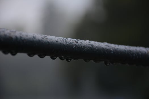 Detailed view of raindrops on a wet steel bar in a moody outdoor setting.