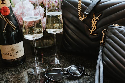 A Close-Up Shot of Glasses of Champagne beside a Saint Laurent Bag