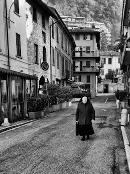 A nun walks through an Italian village street in a striking black and white photograph.