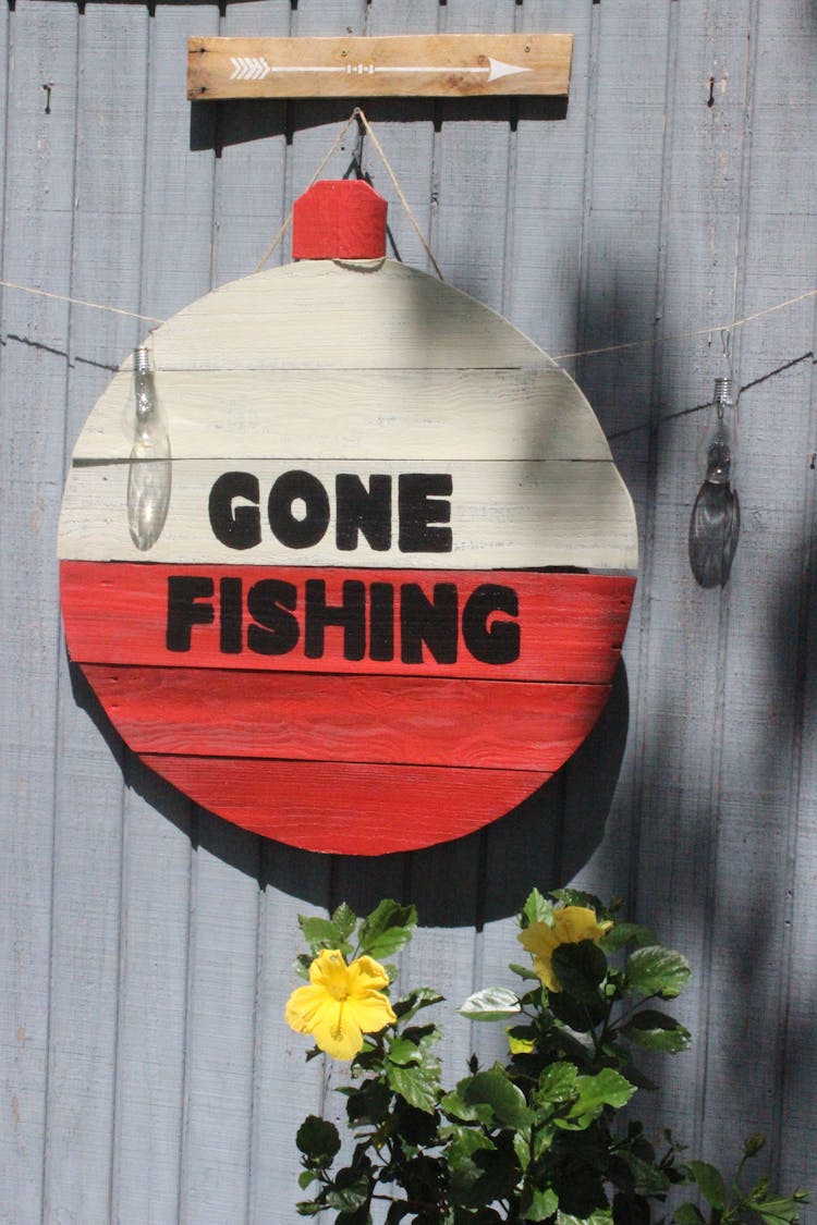 A Gone Fishing Sign On A Red And White Wooden Sign Board Hanging On Gray Wall