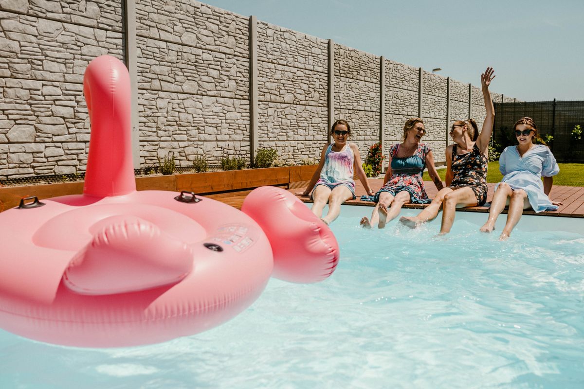 Four women enjoying a sunny day by the pool with a pink float. Stock Photo.
