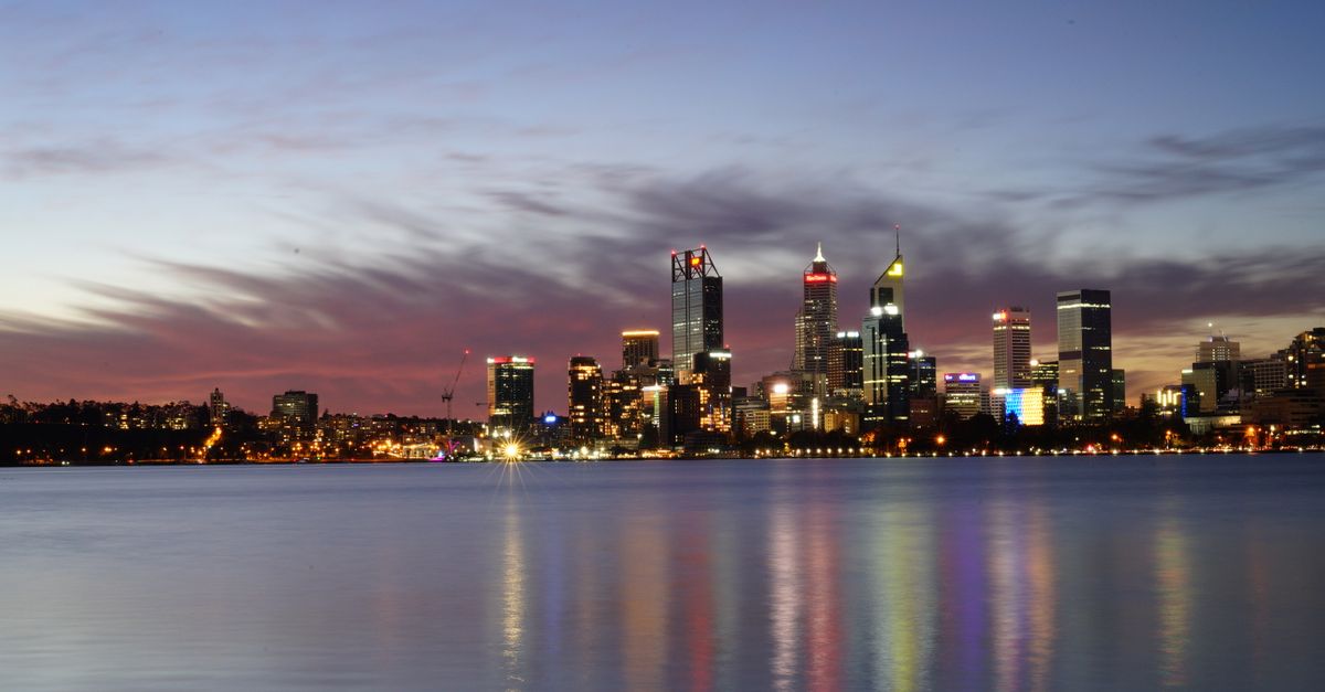 A breathtaking view of Perth's illuminated skyline reflecting on the calm water at dusk.