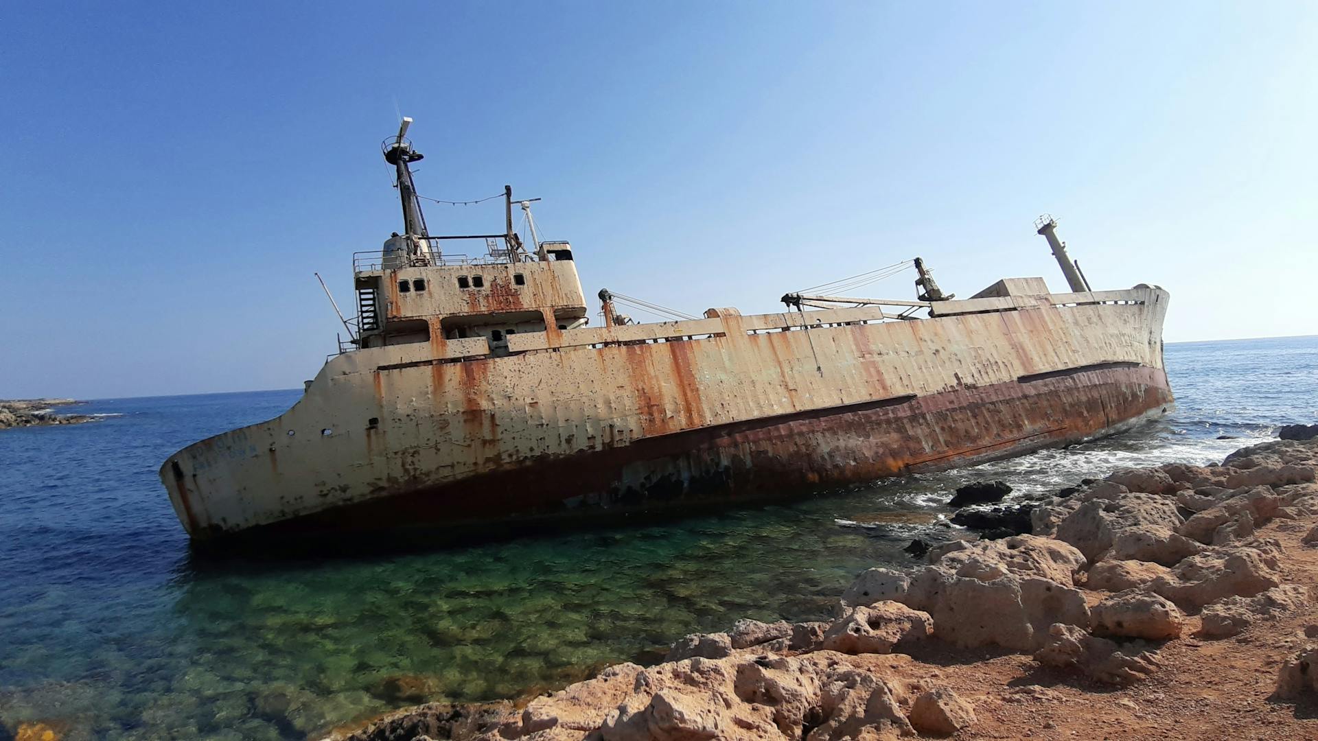 A rusting shipwreck stranded on the rocky coast of Paphos, Cyprus under clear skies.