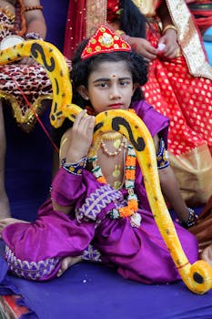 Young child dressed in vibrant traditional attire with snake props, representing cultural festivities.