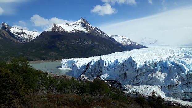 Majestic Perito Moreno Glacier with the Andes Mountains in the background under a bright blue sky.