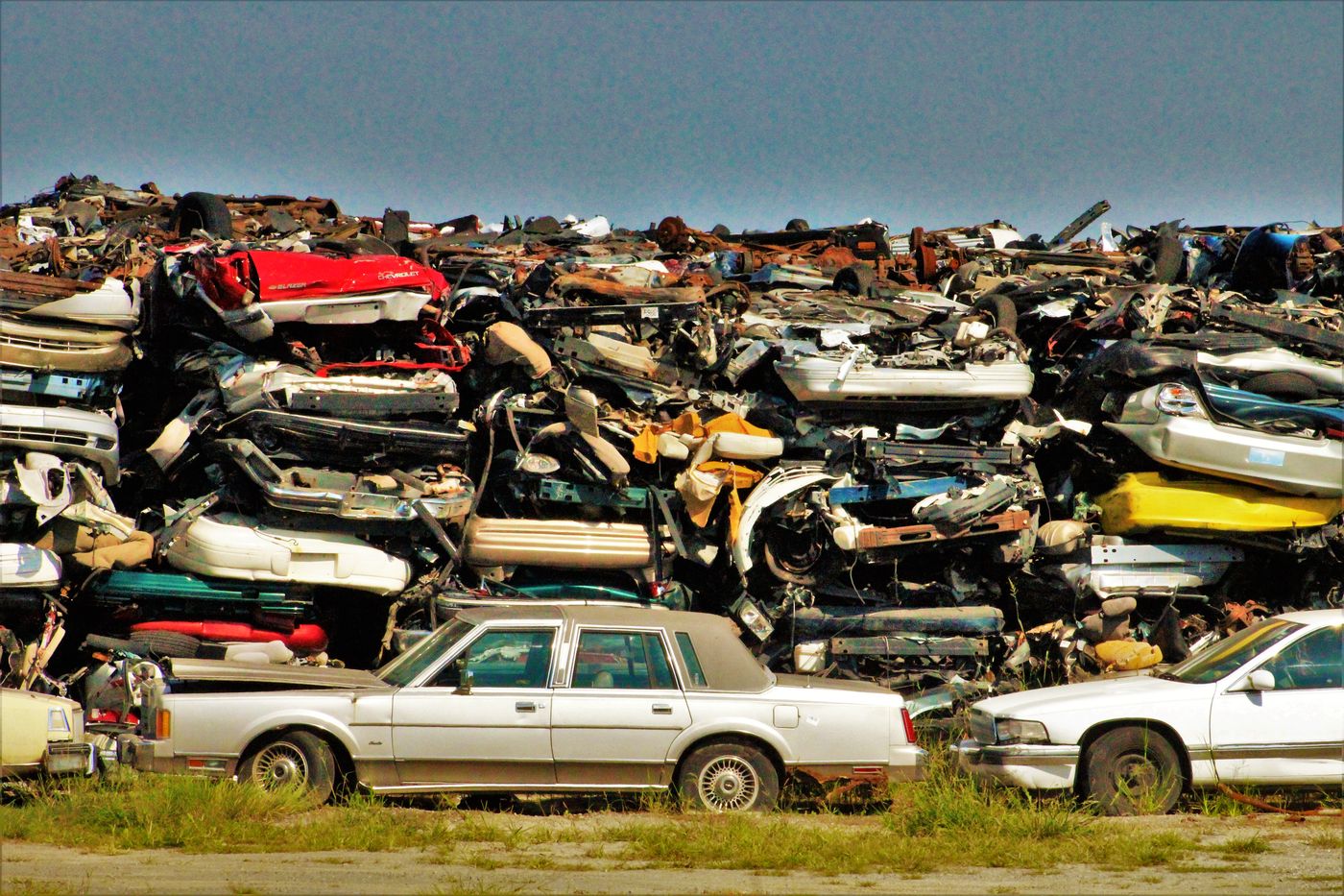 Junk cars sitting in a grass field with weeds grown up around the wheels