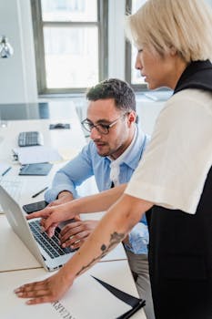 Two professionals engaged in teamwork at an office desk with a laptop.