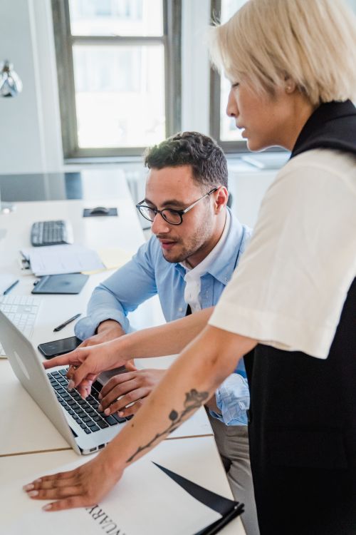 Free Two professionals engaged in teamwork at an office desk with a laptop. Stock Photo