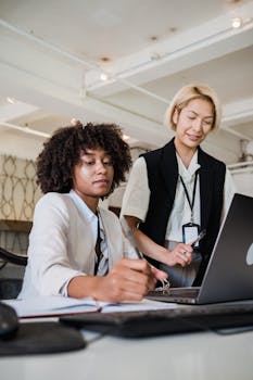 Two diverse businesswomen collaborating on a project in an open office.