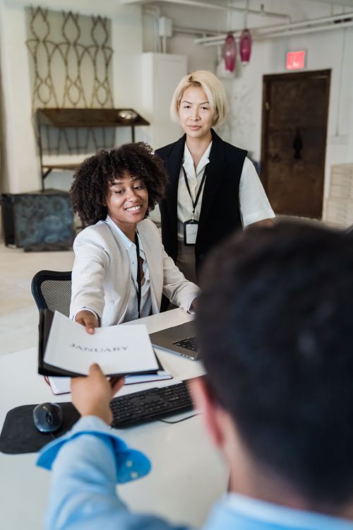 Free Three diverse colleagues collaborate in a modern office environment, exchanging a document. Stock Photo