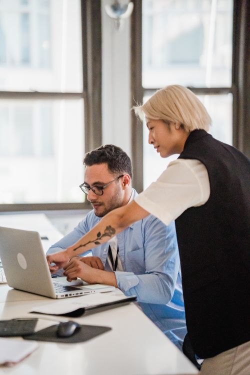 Free A man and woman collaborate on a laptop in a bright office environment, focused and engaged. Stock Photo