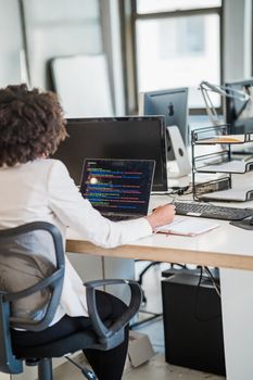 Focused businesswoman coding at desk in a modern office setting, showcasing concentration and technology skills.