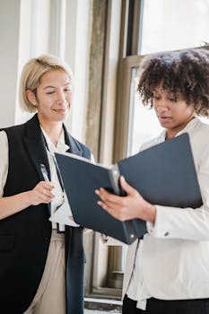 Two diverse businesswomen collaborating on documents in modern office setting.