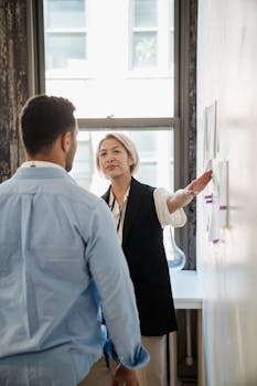 Two professionals discuss strategies at an office wall with project plans.