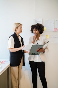 Two professional women discussing documents in a contemporary office environment.