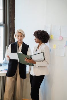 Two professional women reviewing documents in a modern office setting.