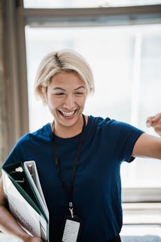 Smiling professional woman in an office, holding documents and expressing confidence.