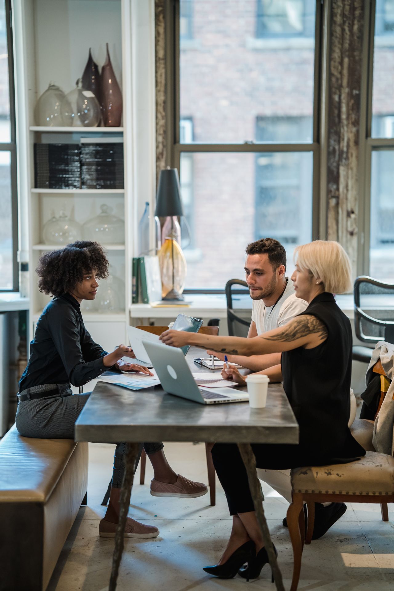 Three diverse adults working together in a modern office, discussing ideas and collaborating at a shared table.