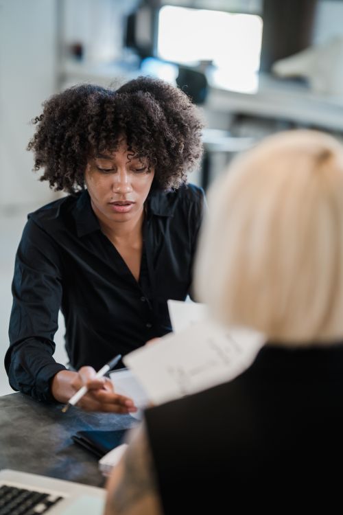 Free Two women collaborate on business documents in a modern office setting. Stock Photo
