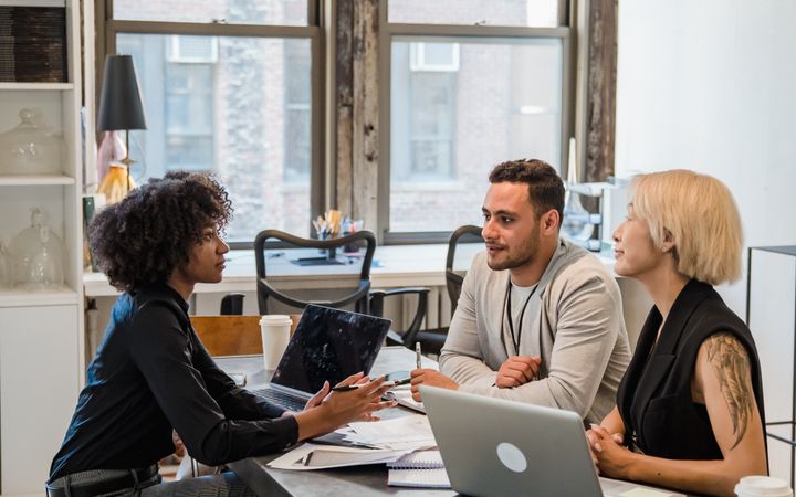 Diverse team collaborating during a meeting in a modern office setting with laptops and notes.