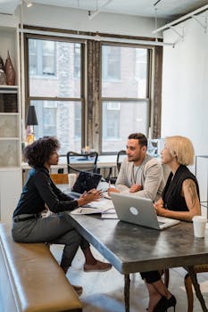 Diverse team collaborating during a meeting in a modern office setting with laptops and notes.