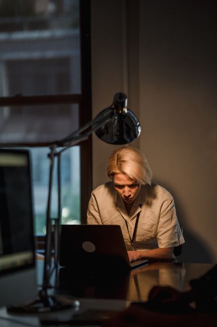 Woman working on a laptop in a dimly lit office setting at night.