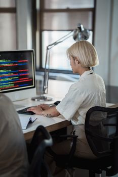 A woman working on a computer at a modern office desk, focused on her task.