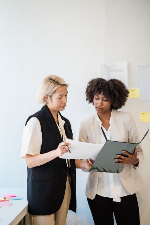 Free Two businesswomen engaged in discussion and document review in an office setting. Stock Photo