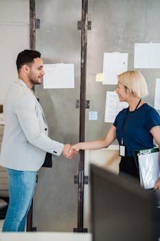 A man and woman shaking hands in a contemporary office environment, symbolizing business collaboration.