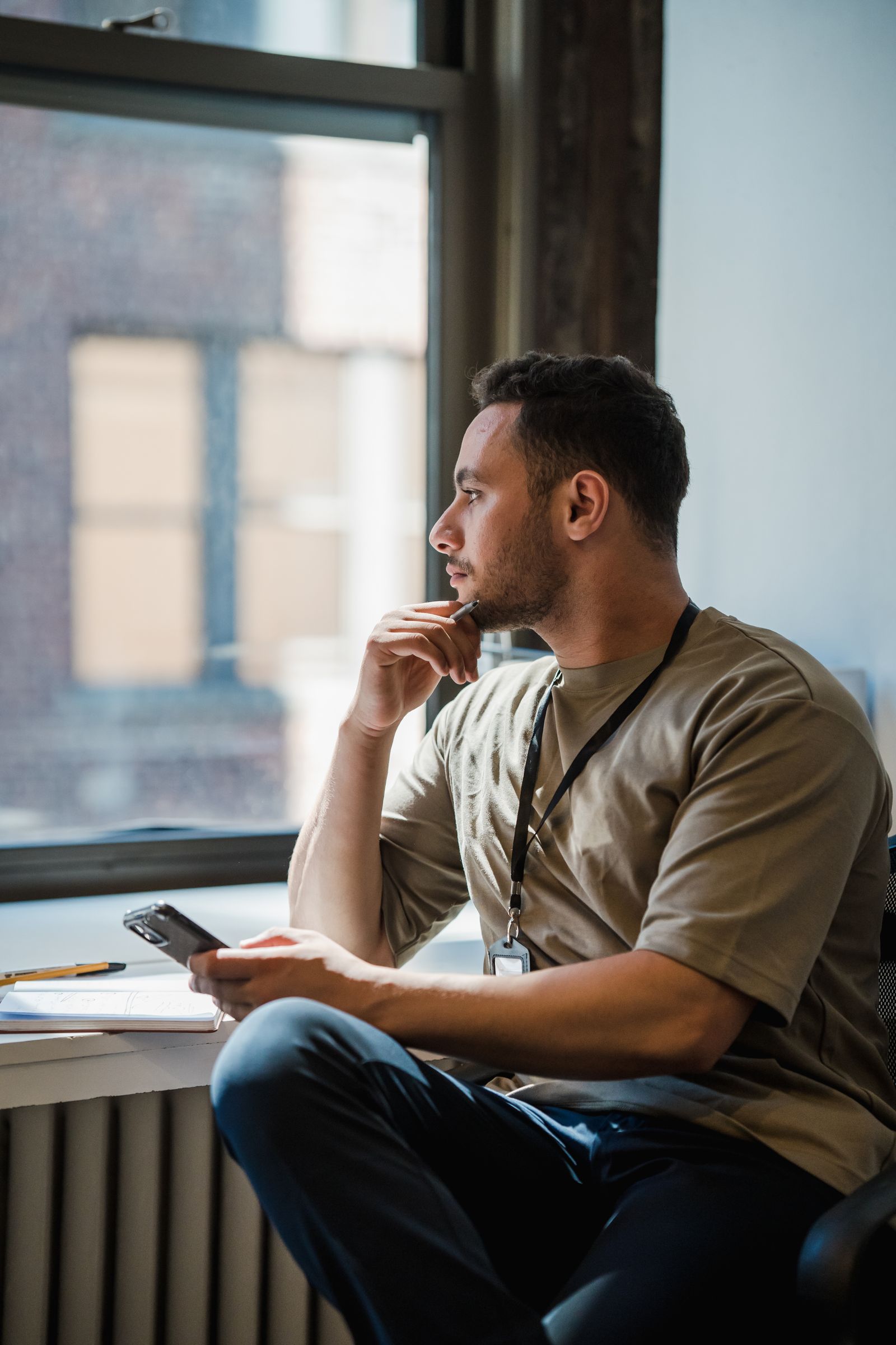 An adult seated beside a window holding a phone