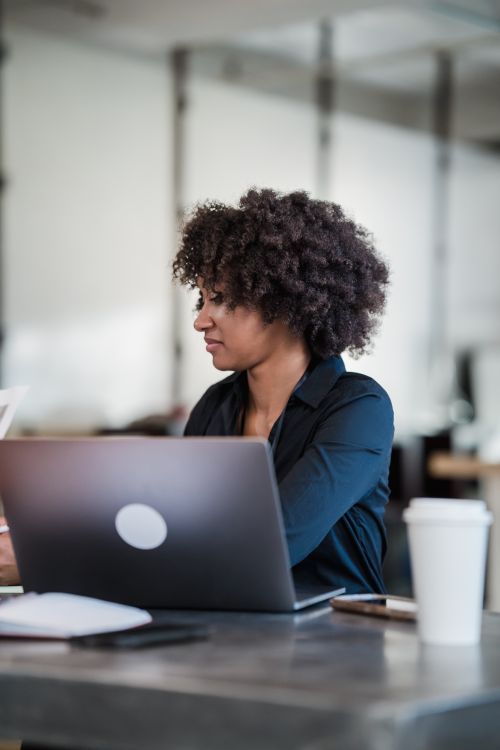 Free Curly-haired woman focused on her laptop in a modern office setting. Stock Photo