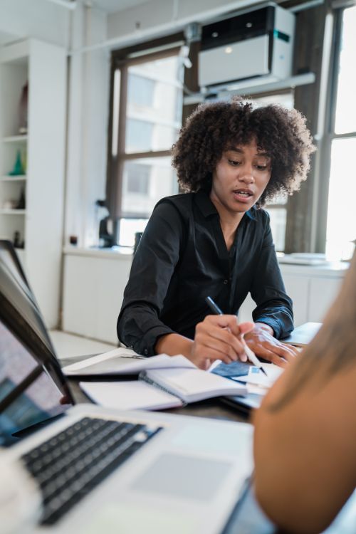 Free A professional woman in office attire taking notes at a modern workspace, engaging in business discussions. Stock Photo