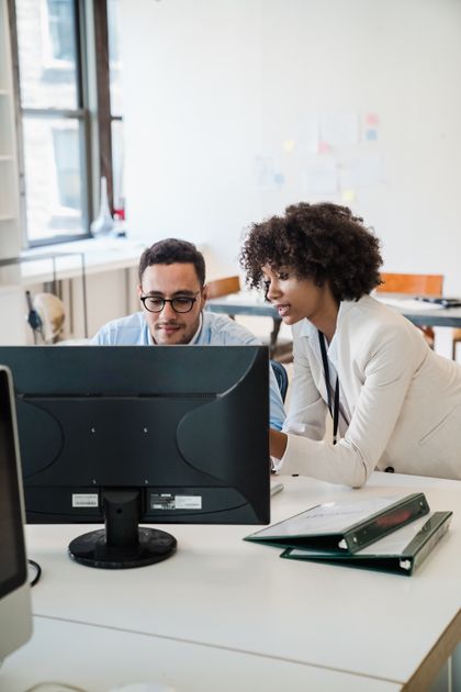 Deux collègues de bureau discutent devant un écran d'ordinateur.