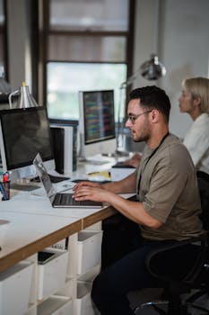 Two professionals focused on their work in a modern office setting with laptops and monitors.