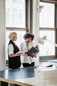 Two businesswomen reviewing documents in a bright office setting.