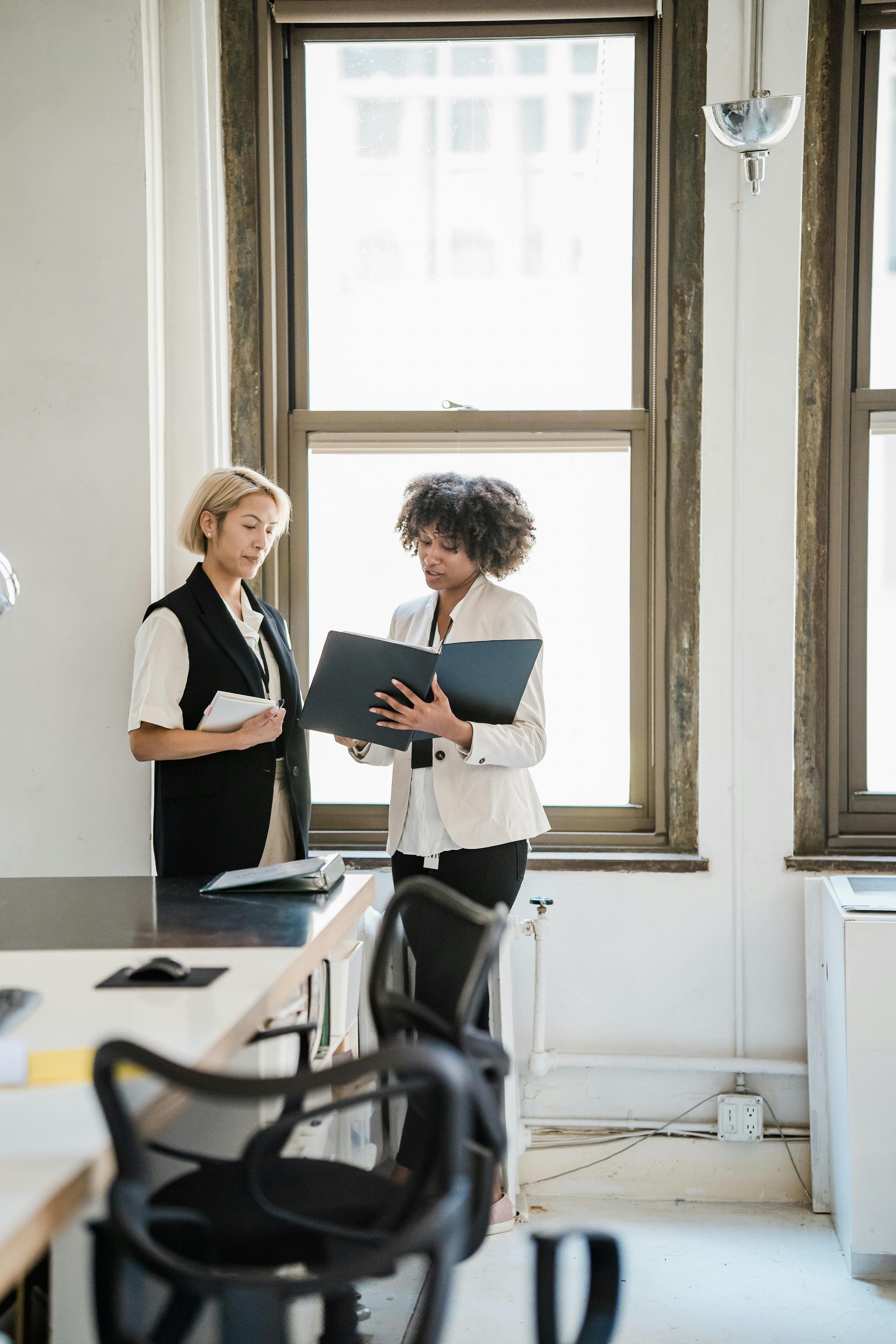 Free Two women discussing work in a bright, modern office setting. Stock Photo