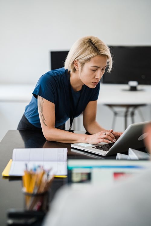 Free Blonde woman concentrates on work at desk using a laptop in modern office setting. Stock Photo